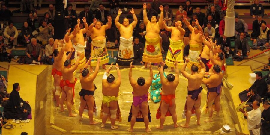 Wrestlers in ceremonial aprons circling the ring before a tournament bout